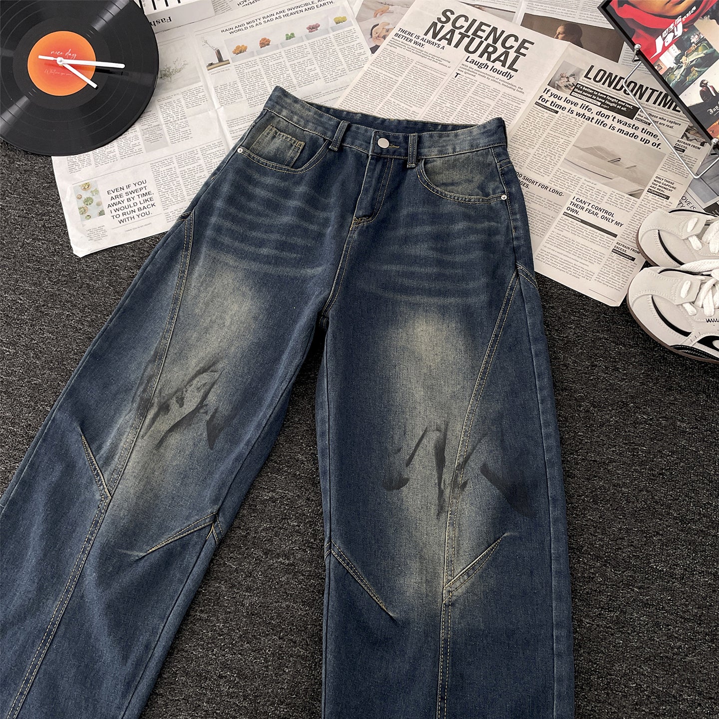 Vaezion Shop streetwear denim jeans with faded wash and abstract print, flat lay on newsprint