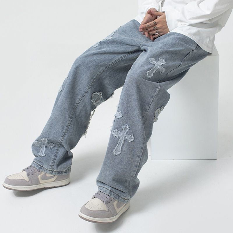 Man in Vaezion streetwear jeans with cross patch details, white shirt, and sneakers