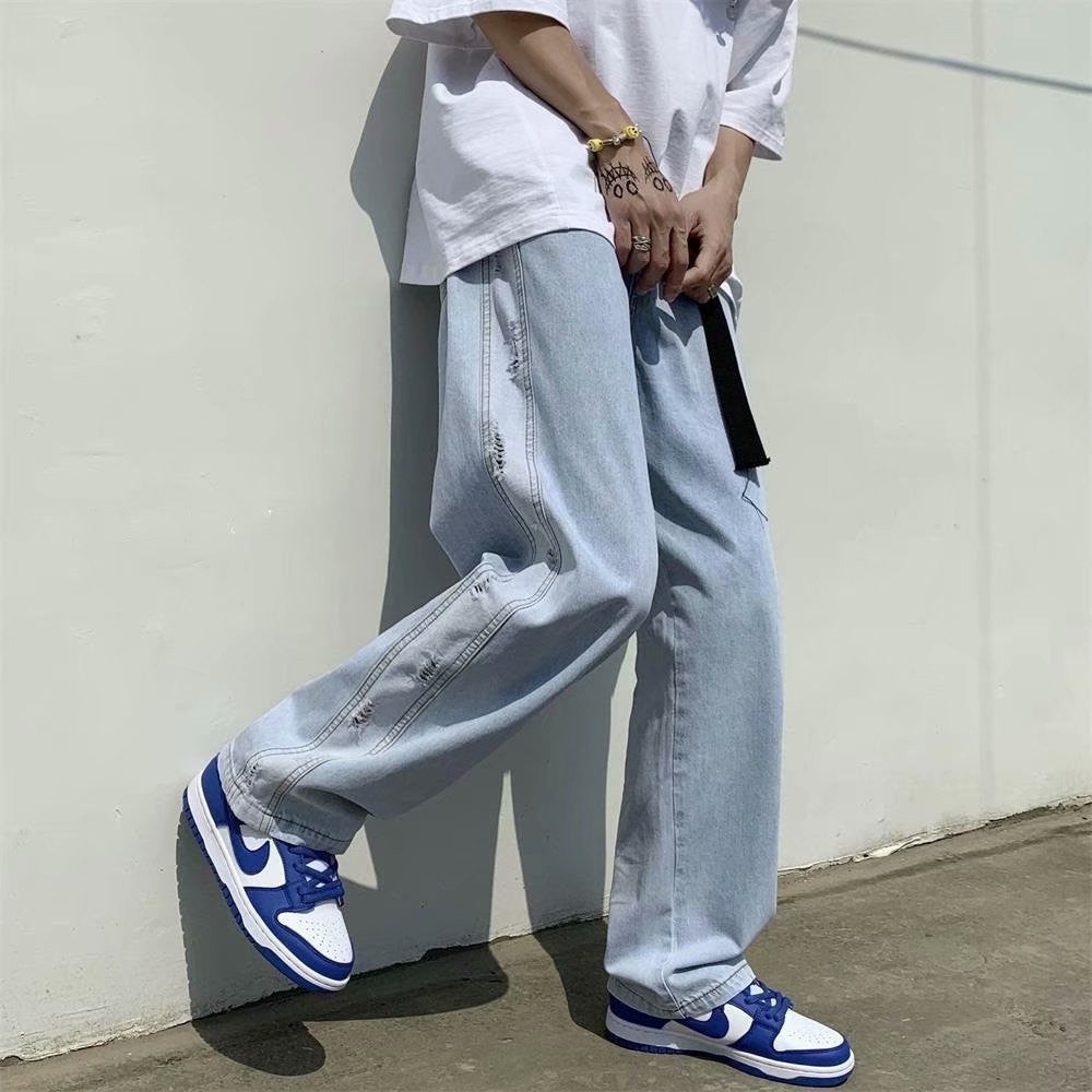 Man in streetwear style with baggy light wash jeans, white T-shirt, blue sneakers, Vaezion fashion